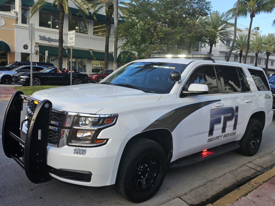 White FPI Security Services SUV parked outside on the street in Florida. It is a sunny day with some cars passing by.