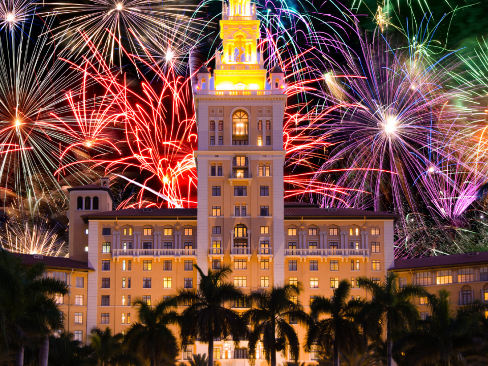 picture of the biltmore hotel in coral gables at night with the lights on, Behind the building are fireworks going off on the 4th of july.