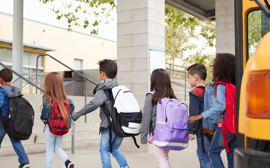 This is a picture of a couple of kids with backpacks on them getting off a yellow school bus. They are entering the school on the left side of the picture.