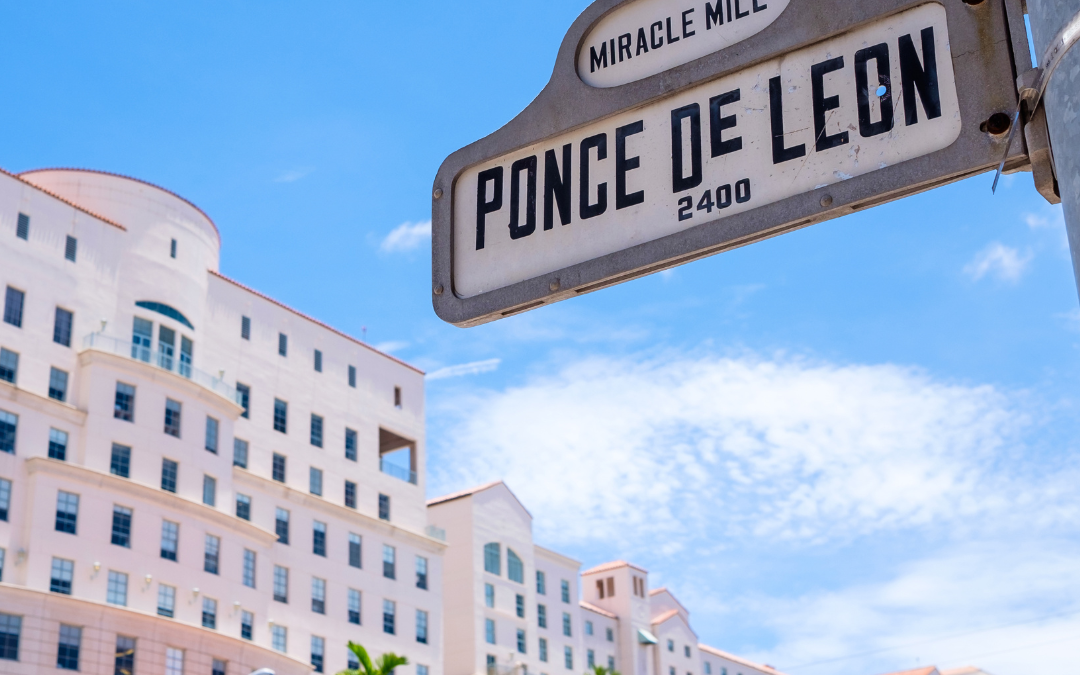 picture of a building in coral gables, florida to the right of the image. to the left there is a sign that says miracle mile ponce de leon 2400. The background is a blue sky.