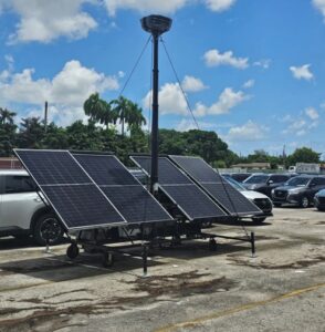 This is an image of the RIO360 security solution with solar panels and two cameras on top of a tall pole in the middle of a car lot. With a sunny day in the background and blue skies. 